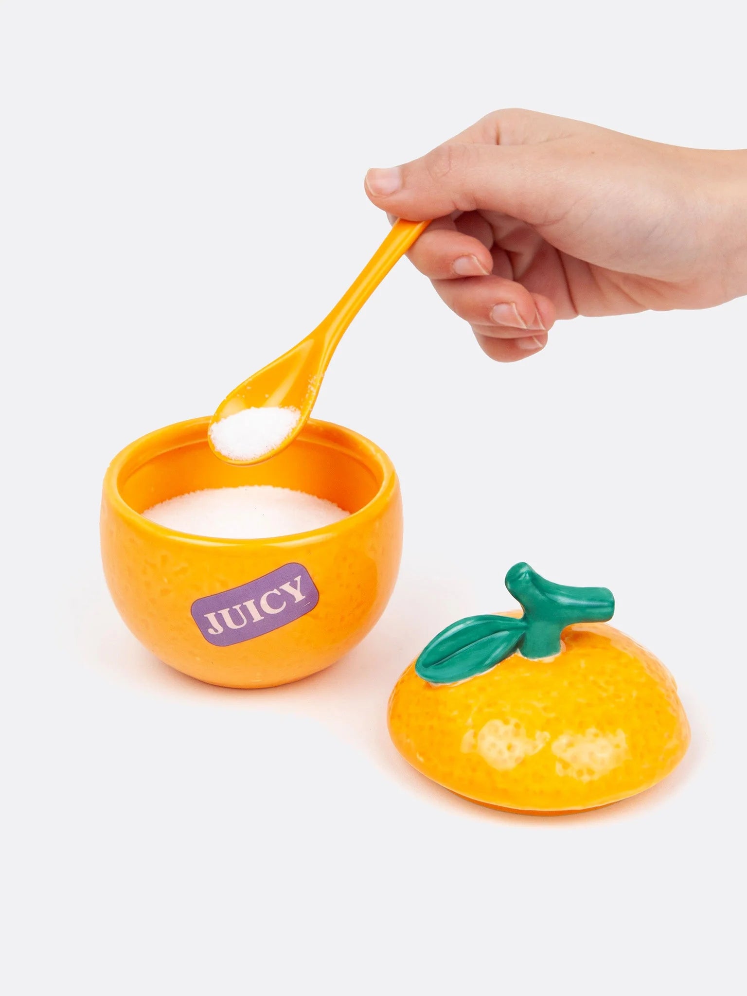 Geöffnete Zuckerdose in Orangenform mit weißem Zucker und Löffel