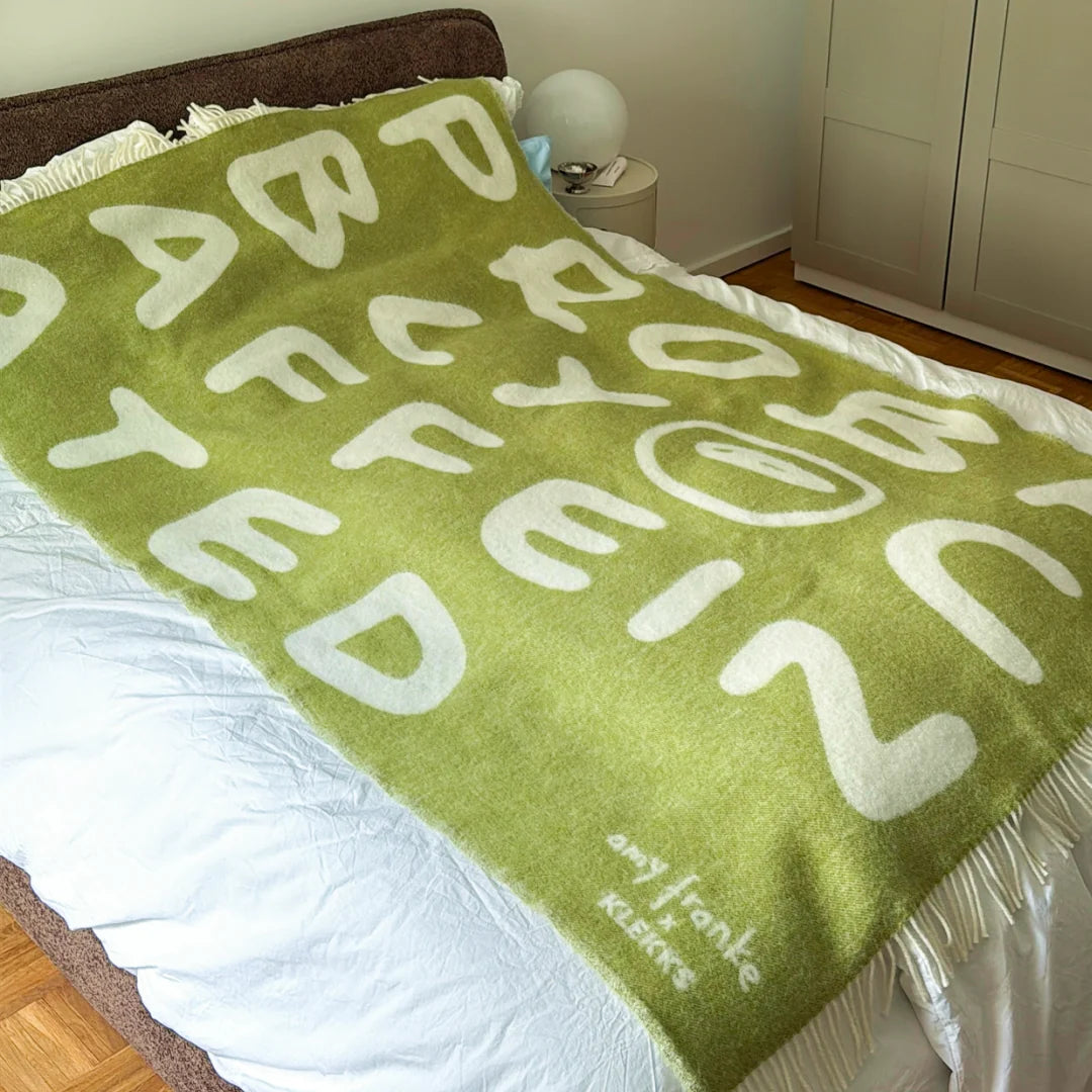 Grüne Wolldecke mit Schriftzug als Tagesdecke auf einem Bett