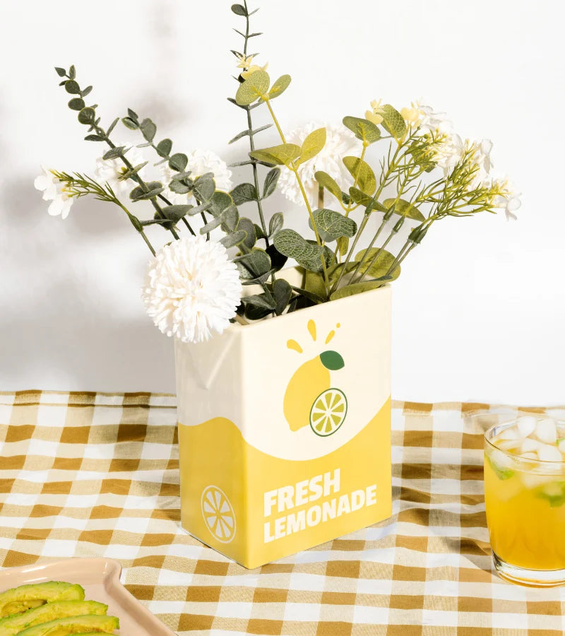 Gelbe Keramikvase in Saftkartonform mit weißem Blumenstrauß